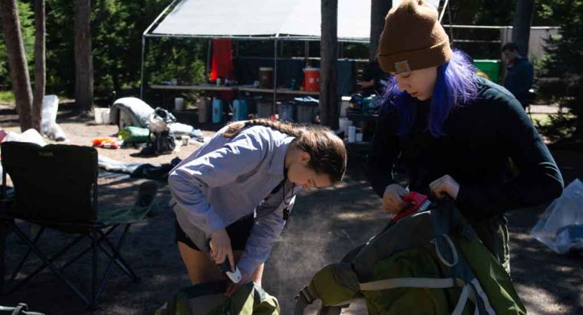 two teens girls packing backpacks in preparation for outward bound backpacking expedition 